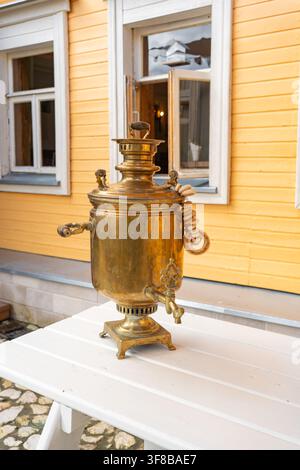 Vintage-traditioneller Samowar auf einem Holztisch im Freien vor einem rustikalen Holzhaus. Perfektes Stockfoto für ethnische Reisen, Teetraditionen und Stockfoto