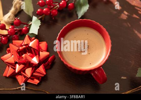 Rote muschelförmige Tasse steht auf dunklem Holztisch, zeigt Crema und kleine Blasen mit roter Schleife. Tasse, Kaffee, festlich, Stillleben, Fotografie, Küche, h Stockfoto