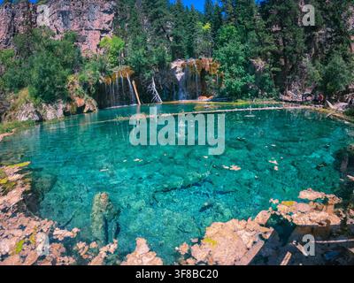 Kristallklares Wasser sammelt sich unter einem kaskadierenden Wasserfall. Üppige grüne Bäume umrahmen die ruhige Naturszene. Felsen umgeben den Pool und zeigen die Natur Stockfoto