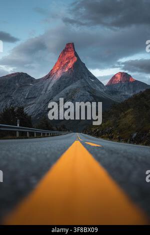 Blick auf den ikonischen Stetind-Berg, der vom goldenen Licht des Sonnenuntergangs am Ende einer kurvenreichen Asphaltstraße in der Gemeinde Narvik, Nordland, Norwegen, beleuchtet wird. Stockfoto