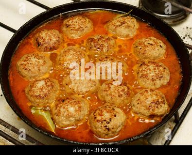 Fleischbällchen in Tomatensoße auf einem Herd in einer Küche kochen Stockfoto