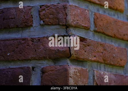Verwitterte Ziegelwand zeigt sichtbare Risse. Rustikale Textur verleiht der Struktur Charakter und Alter. Nahaufnahme hebt Mörtel- und Ziegelunregelmäßigkeiten hervor. Stockfoto