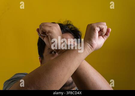 Kraftvolles Porträt eines jungen asiatischen Mannes, der die Arme in einer starken Abwehrhaltung verschränkt vor einem soliden gelben Hintergrund. Der entschlossene Mensch formt Stockfoto