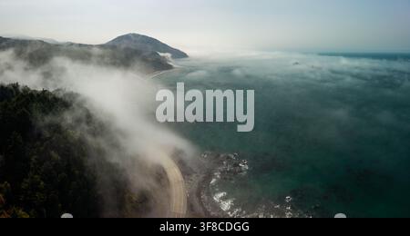 Luftaufnahme der Highway 101, die sich entlang der nebligen Küste Oregons mit dichtem Wald und dem Pazifischen Ozean in Port Orford, Oregon, Vereinigte Staaten schlängelt Stockfoto