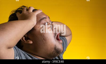 Dynamisches Profilporträt eines jungen asiatischen Mannes, der extreme Frustration oder Panik gegen einen leuchtend gelben Hintergrund ausdrückt. Der verängstigte Mensch Stockfoto