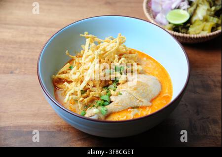 Traditionelle nordthailändische Kokosnuss-Kurry-Nudelsuppe mit Hühnerdrumstick, garniert mit knusprigen Eiernudeln in einer blauen Schüssel. Stockfoto