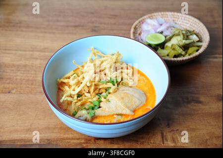 Traditionelle nordthailändische Kokosnuss-Kurry-Nudelsuppe mit Hühnerdrumstick, garniert mit knusprigen Eiernudeln in einer blauen Schüssel. Stockfoto