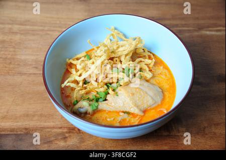 Traditionelle nordthailändische Kokosnuss-Kurry-Nudelsuppe mit Hühnerdrumstick, garniert mit knusprigen Eiernudeln in einer blauen Schüssel. Stockfoto