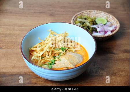 Traditionelle nordthailändische Kokosnuss-Kurry-Nudelsuppe mit Hühnerdrumstick, garniert mit knusprigen Eiernudeln in einer blauen Schüssel. Stockfoto