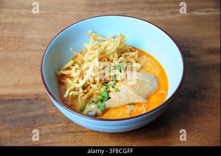 Traditionelle nordthailändische Kokosnuss-Kurry-Nudelsuppe mit Hühnerdrumstick, garniert mit knusprigen Eiernudeln in einer blauen Schüssel. Stockfoto