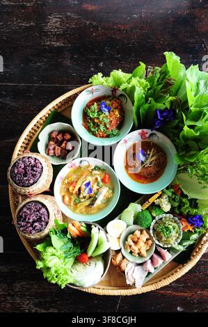 Oberansicht von traditionellem nordthailändischem Essen, Set Khantoke, serviert auf rundem gewebtem Tablett über dunklem Holzgrund. Stockfoto