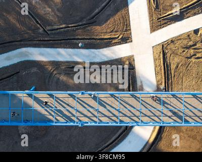 Luftaufnahme einer blauen Fußgängerbrücke mit Menschen, die darüber gehen, vor dem Hintergrund von Erdwegen und Bauarbeiten in Belgrad, Serbien. Stockfoto