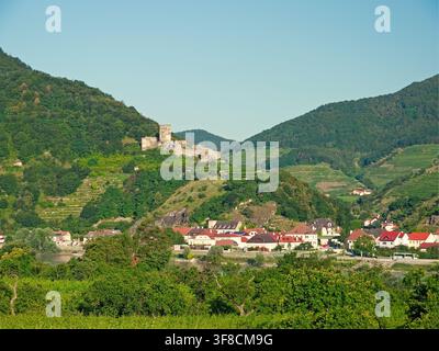 Sankt Lorenz, Österreich - 05.07.2016: Historische Burgruinen auf einem terrassierten Weinberghang über einer kleinen Stadt und einem Fluss unter einem klaren blauen Himmel Stockfoto