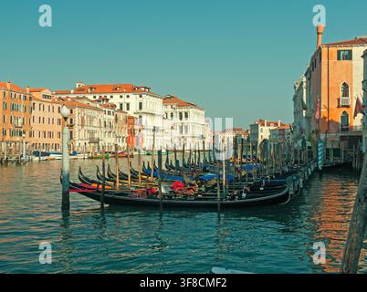 San Polo, Venedig, Italien - 10.07.2016: Traditionelle schwarze Gondeln, die entlang eines Kanals mit farbenfrohen historischen Gebäuden unter einem klaren blauen Himmel vertäut sind Stockfoto