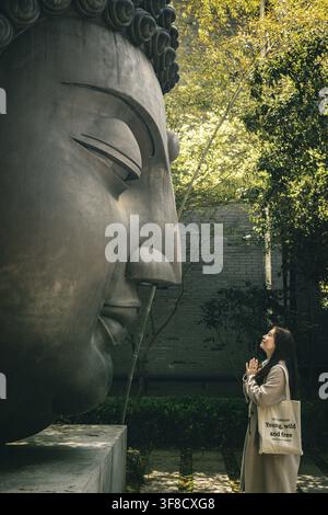 Frau mit Händen im Gebet vor riesiger Buddha-Kopf-Statue, Botanischer Garten Hangzhou Stockfoto