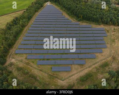 Luftaufnahme einer großen dreieckigen Solarfarm, umgeben von üppigen grünen Bäumen und Feldern in den Niederlanden. Stockfoto
