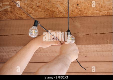 Nahaufnahme von menschlichen Händen, die eine warme Lichterkette aus dekorativen Glühbirnen von der Decke hängen, Konzept für die Inneneinrichtung des Hauses. Hochwertiges Foto Stockfoto