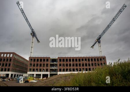 Ansicht einer Baustelle mit zwei großen Turmkranen und neuem Ziegelbaugerüst unter einem bewölkten Himmel Stockfoto