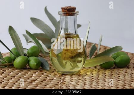 Glasflasche mit extra nativem Olivenöl mit grünen Oliven und Blättern Stockfoto