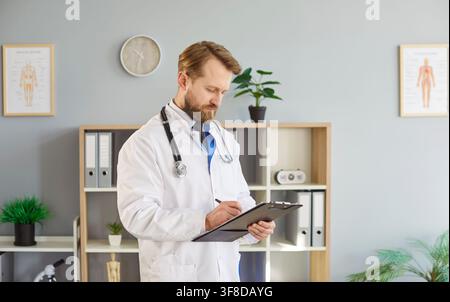 Arzt oder Allgemeinmediziner schreibt Notizen auf, hält ein Klemmbrett, posiert in einer Arztpraxis Stockfoto
