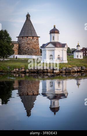 Blick auf das historische Solowezki-Kloster mit seinem Steinturm und der weißen Kapelle, die sich im ruhigen Wasser der Bucht in Solowezki, Oblast Archangelsk, spiegelt Stockfoto
