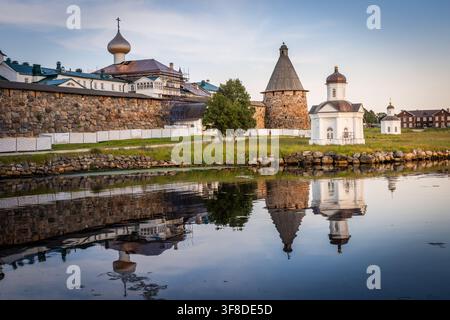 Blick auf das Solowetski-Kloster mit seinen massiven Steinmauern, Zwiebeltürmen und Türmen, die sich im ruhigen Wasser der Bucht in Solowetski, Arkhangelsk O spiegeln Stockfoto