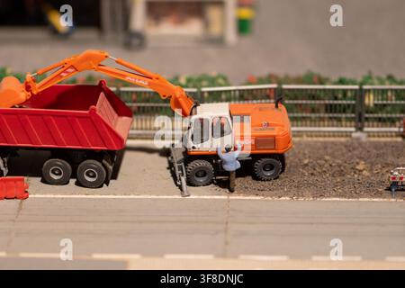 WIEN, ÖSTERREICH, 26. November 2022: Eine Nahaufnahme einer Dioramaszene zeigt einen Miniatur-Orange-Bagger neben einem roten Kipper mit einer kleinen Arbeiterfigur daneben Stockfoto