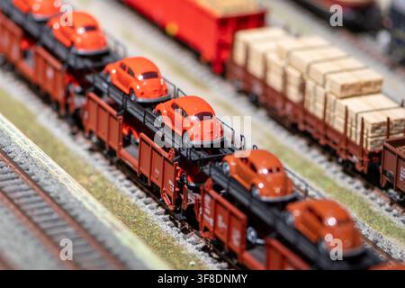 WIEN, ÖSTERREICH, 26. November 2022: Nahaufnahme einer Modelleisenbahn-Güterzuggarnitur, die kleine orangefarbene Spielzeugautos auf Flachwagen neben einem anderen transportiert Stockfoto
