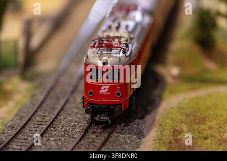 WIEN, ÖSTERREICH, 26. November 2022 : Ein rotes elektrisches Miniatur-Lokomotivmodell wird frontal auf detaillierten Bahngleisen fotografiert, mit einem verschwommenen Hintergrund Stockfoto