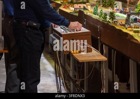 WIEN, ÖSTERREICH, 26. November 2022: Ein mittelalter Mann steht neben einer Steuerbox und bedient eine detaillierte Modelleisenbahnanlage in Innenräumen. Stockfoto