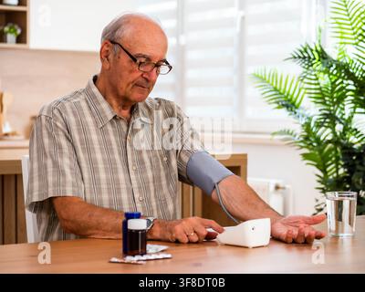 Senior Mann überprüft seinen Blutdruck, während er zu Hause am Tisch sitzt. Stockfoto