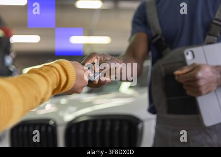 Mechaniker und zufriedener Kunde in einer modernen Autowerkstatt. Autoschlüssel werden nach abgeschlossener Wartung und Reparatur zurückgegeben. Stockfoto