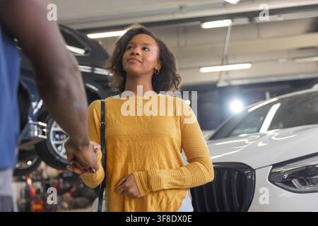 Professioneller Service und Kundenzufriedenheit in einer Autowerkstatt, ein Mechaniker schüttelt die Hand eines lächelnden Besitzers. Stockfoto