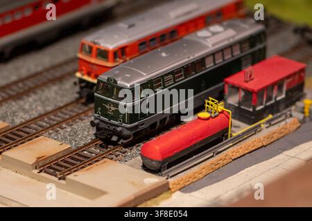 Eine Nahaufnahme zeigt Miniatur-Diesellokomotiven auf einem detaillierten Modellbahngleis neben einem roten Kraftstofftank und einer kleinen Wartungsstruktur. Stockfoto