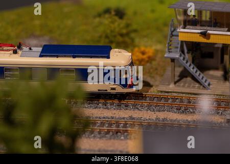 Ein blaues und cremefarbenes Modellzug steht auf Schienen neben einem detaillierten Miniatur-Eisenbahnverkehrsturm in einer Dioramaszene. Stockfoto