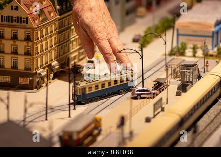 WIEN, ÖSTERREICH, 26. November 2022: Eine Nahaufnahme zeigt eine ältere Hand, die eine Miniaturstraßenbahn in einer detaillierten Stadtszenen-Modellbahn berührt. Stockfoto