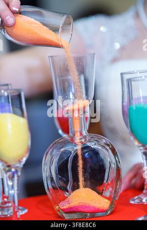 Eine Braut gießt Orangensand aus einem Glas in einen Dekanter während einer traditionellen Hochzeits-Sand-Zeremonie. Stockfoto