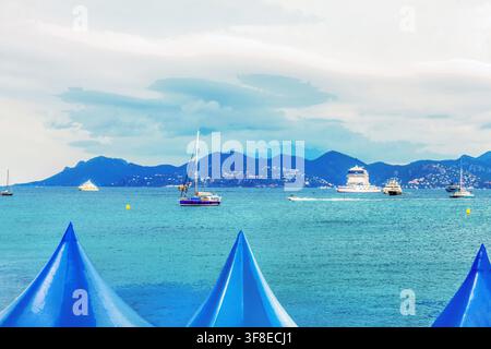 Panoramablick auf die Bucht in Cannes - Frau, die hinter einem Schnellboot und mehreren Motoryachten oder Segelbooten vor Anker fährt und ein riesiges Kreuzfahrtschiff im d Stockfoto