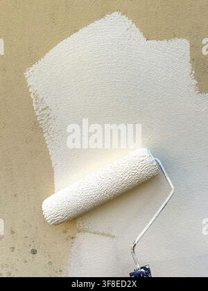 Nahaufnahme von glatter weißer Mauerfarbe, die mit einem Farbroller auf eine Außenwand aufgetragen wird. Stockfoto