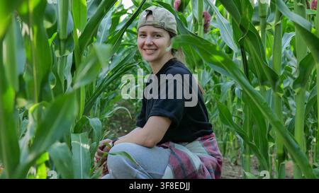 Frau sitzt zwischen Maispflanzen auf einem landwirtschaftlichen Feld Stockfoto