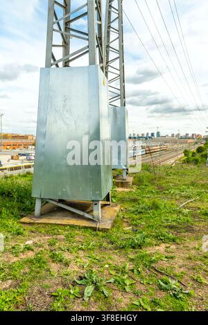 Silberne Elektroschränke am Fuße eines Übertrachtungsturms mit Blick auf Bahngleise und eine entfernte städtische Skyline. Stockfoto