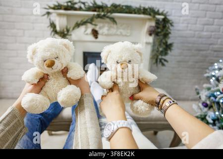 Ein Paar hält glücklich zwei kleine weiße Teddybären vor einem gemütlichen Kamin und Weihnachtsbaum. Stockfoto