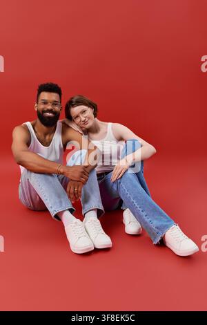 Paar in trendigen Outfits teilt einen süßen Moment zusammen vor einem roten Hintergrund. Stockfoto