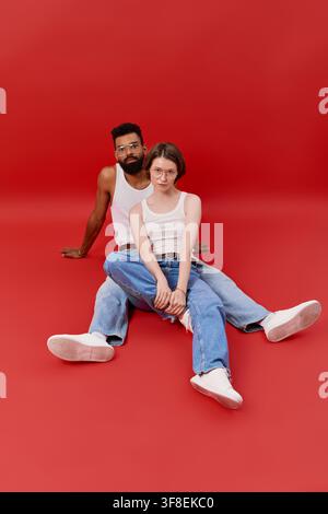 Verliebtes Paar in stilvollen Outfits, das die gemeinsame Gesellschaft gegen einen kräftigen roten Hintergrund genießt. Stockfoto