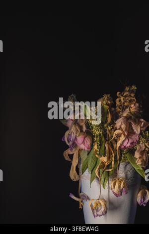 Getrocknete rosa Blumen, die über eine weiße Keramikvase fallen, Stillleben mit schwarzem Hintergrund Stockfoto