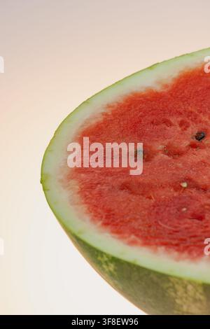 Nahaufnahme einer frisch geschnittenen roten Wassermelone, die saftiges Fruchtfleisch und schwarze Samen auf einem hellen Hintergrund zeigt. Stockfoto