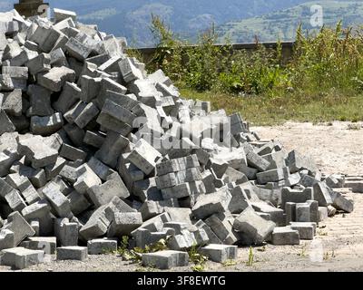 Ansicht eines großen Haufens grauer Betonpflastersteine, die im Freien in einer ländlichen Umgebung mit grasbewachsenen Hügeln im Hintergrund in Posof, Ardahan, Turkiye gestapelt sind Stockfoto