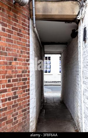 Schmale überdachte Passage zwischen historischen Backsteingebäuden in York, England, mit verwitterten Wänden und traditionellem Steinpflaster Stockfoto