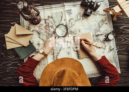 Ansicht von oben von Frau Notizen in Notebook mit leeren Umschläge, Karte und Foto Kamera auf Holz- Oberfläche Stockfoto
