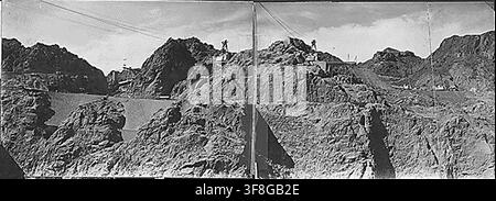 Eine Fotografie aus dem Jahr 1933 vom Canyonrand oberhalb der Baustelle des Hoover Damms auf der Nevadaschen Seite, die den Betriebsturm für den 150-Tonnen-Seilzug, die Hochofen-Betonmischanlage der Six Companies und die Seilzugbetriebe über die Dammstelle, die Wassereinlasstürme und die Überlaufbauwerke zeigt, mit Steinschützer-Stützmauern, Ausgrabungen am oberen Widerlager und Ausgrabungen an den oberen Wassereinlasstürmen im Vordergrund, während des Baus des Hoover Damms in Boulder City, Nevada. Stockfoto